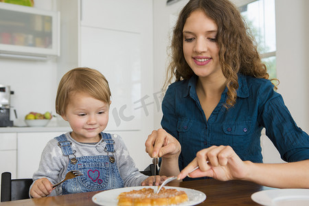 儿童培育摄影照片_十几岁的女孩在餐桌上为蹒跚学步的女孩子切蛋糕