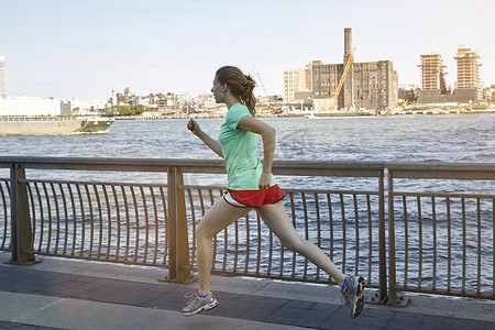 美国纽约市一名年轻女子在户外锻炼在河边跑步