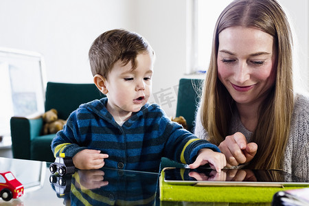 中年妇女和男婴在餐桌上使用数字平板电脑上的触摸屏