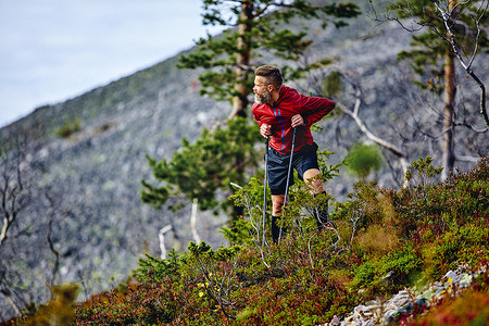 芬兰拉普兰一名男子倚靠在徒步旅行的杆子上回望陡峭的山丘