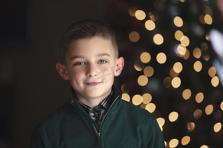 圣诞树亮摄影照片_圣诞树前男孩微笑着看着相机的肖像