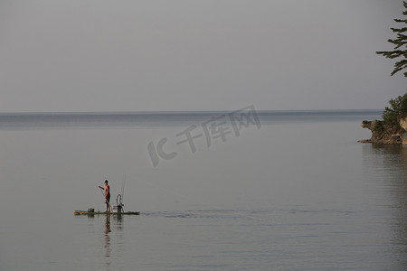 在美国密歇根州奥特林湾的苏必利尔湖十几岁的男孩在冲浪板上钓鱼的远景
