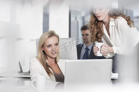 女商人在办公室使用笔记本电脑同事在后台使用电脑