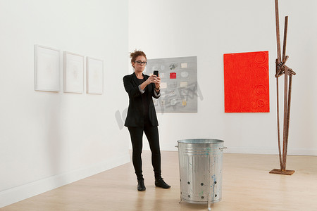一名年轻女子用手机为画廊里的艺术品拍照