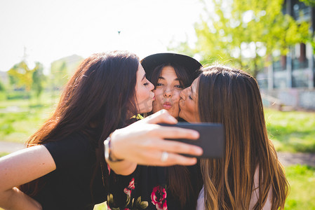 三位年轻女性朋友在公园亲吻智能手机自拍