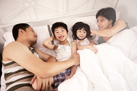 年轻的中国家庭父母和两个年幼的孩子一起躺在家里的床上