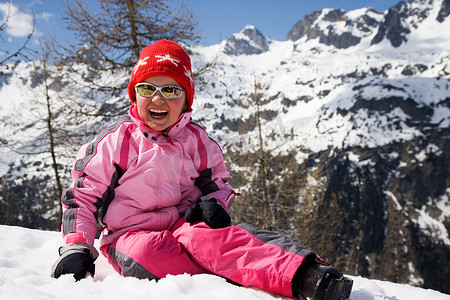 坐在雪地里摄影照片_穿着粉色衣服的女孩坐在雪地里