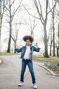 跳绳动作摄影照片_女孩玩着跳绳看着摄像机举起手臂