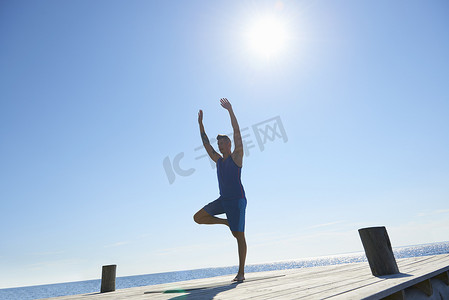 一名男子在码头上单腿站立举起双臂锻炼