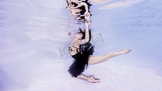 穿着芭蕾舞短裙和芭蕾舞鞋的女子在水下观看手打破水面