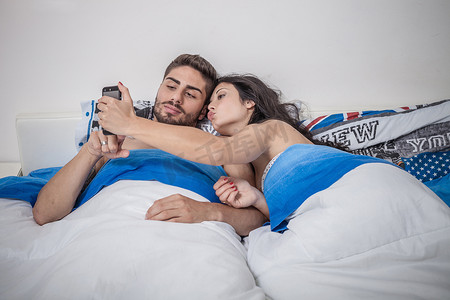 家庭时间摄影照片_一对年轻夫妇在床上用智能手机自拍