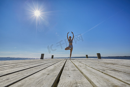 举起武器摄影照片_中远处码头上的女人单腿站立手臂高高举起