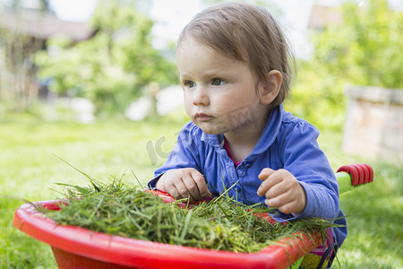花园里可爱的小女孩靠在玩具手推车上的肖像