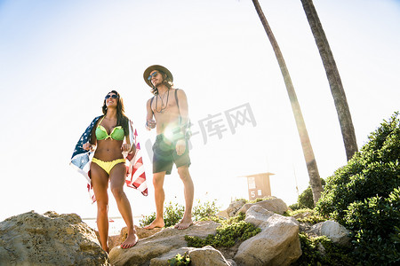 美国加利福尼亚州纽波特海滩披着美国国旗的年轻夫妇从岩石上眺望