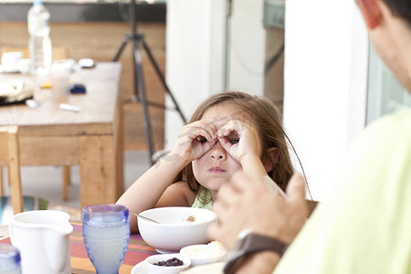 家庭餐摄影照片_父女俩坐在早餐桌旁女儿用手指做望远镜
