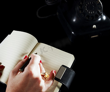 写字的的手摄影照片_一名妇女通过电话在笔记本上写字