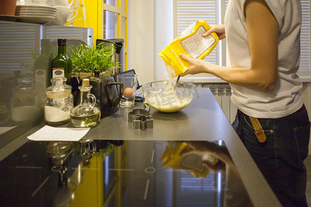 中年妇女将面粉倒入厨房柜台的搅拌碗中