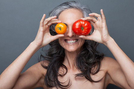 成熟的女人用红黄相间的西红柿遮住眼睛