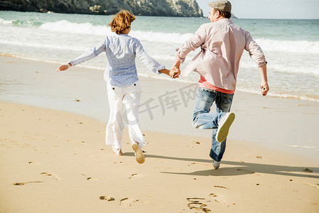 在法国布列塔尼的卡马雷特苏尔梅尔海滩上一对成年夫妇手牵手在海滩上奔跑
