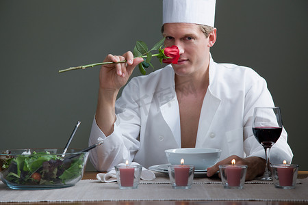 一名身着厨师服装的男子闻着玫瑰花的香味享受着浪漫的晚餐