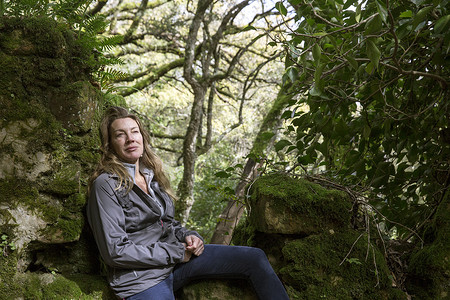 西班牙女摄影照片_女徒步旅行者坐在长满苔藓的林地岩石上西班牙