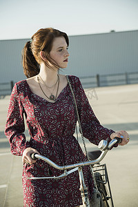 城市漫步摄影照片_一名年轻女子在空荡荡的停车场推着自行车