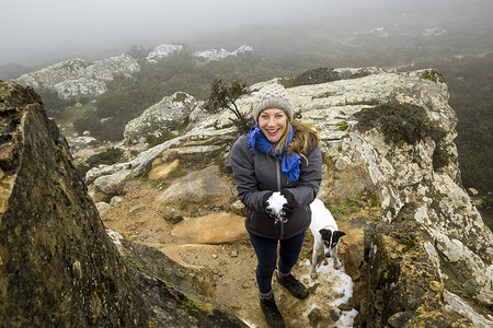 西班牙雾蒙蒙的山上女徒步旅行者和她的狗拿着雪球的肖像