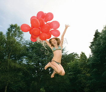 戴着红色气球的女孩在花园里跳跃