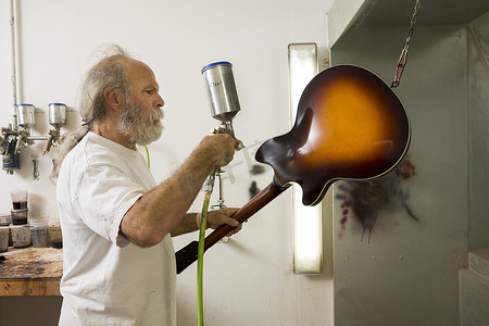 喷枪柔边画笔摄影照片_车间里的吉他制造者使用喷枪给吉他上漆