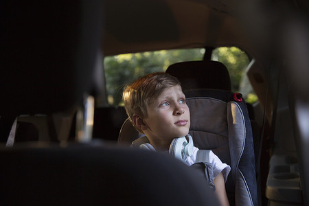 窗户看外面摄影照片_坐在车后座上的男孩透过车窗凝视着外面