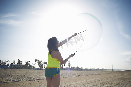 举起武器摄影照片_海滩上的女人的后视线用泡泡棒做泡泡的胳膊高高举起
