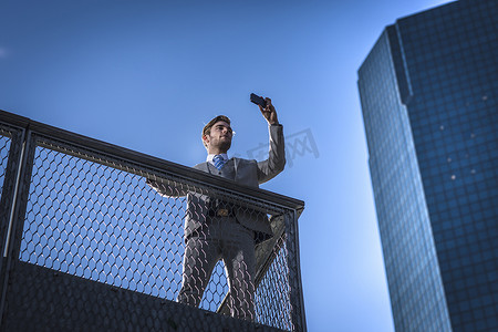 美国纽约在城市阳台上用智能手机自拍的年轻商人的低角视角