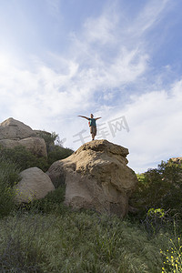 举起武器摄影照片_女徒步旅行者在岩石上举起手臂