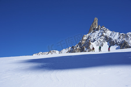 三名滑雪者在法国格拉尼亚阿尔卑斯山的勃朗峰上滑行的远景