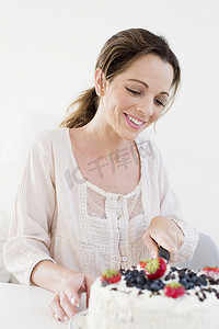 成年了摄影照片_成熟女子用刀切水果包蛋糕低头微笑