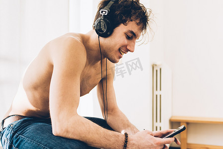 一名戴着耳机的裸胸男子微笑着低头看着智能手机