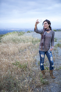 一名年轻女子在乡村山丘上摆姿势自拍智能手机