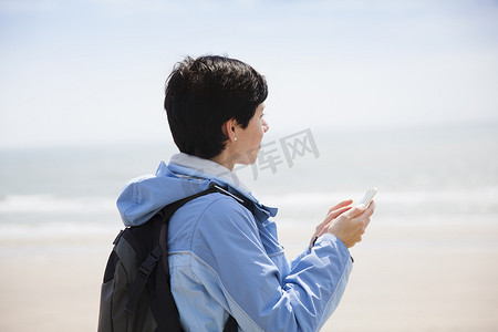 高尔夫球包摄影照片_中年妇女一边在海滩上用智能手机发短信一边眺望大海