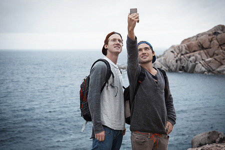 意大利撒丁岛科斯塔·斯梅拉达年轻男子在海边用智能手机微笑自拍