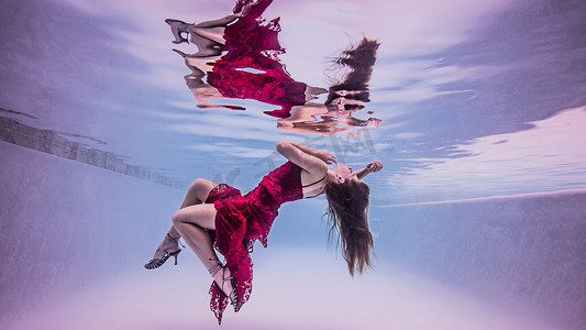 穿着红色连衣裙和高跟鞋的女孩漂浮在水面上的水下景象