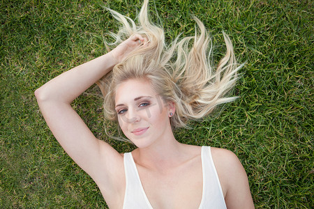 双手放在脑后摄影照片_躺在草地上的微笑的女人