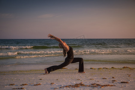 日落时分成熟的女子在海滩上练习瑜伽
