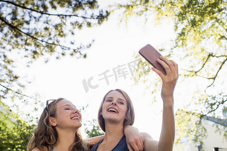 十几岁的少女摄影照片_公园里两名十几岁的女孩在用智能手机自拍