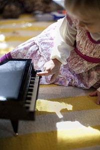 月球音乐盒摄影照片_圣诞节坐在客厅地板上玩玩具钢琴音乐盒的女孩子