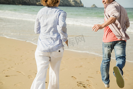 在法国布列塔尼的卡马雷特苏尔梅尔海滩上奔跑的成熟夫妇