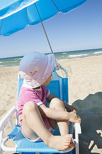 走神摄影照片_从沙滩椅上仰望大海的蹒跚学步的女孩