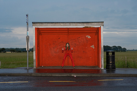 路边垃圾桶摄影照片_十几岁的女孩在红色公交车站穿着红色衣服