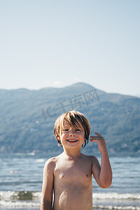 第十一摄影照片_意大利伦巴第路易诺海滩和山脉上的赤裸上身的男孩微笑着看着相机