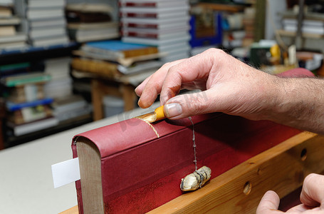 老年男性传统装订师将金叶贴在书脊上的手部特写