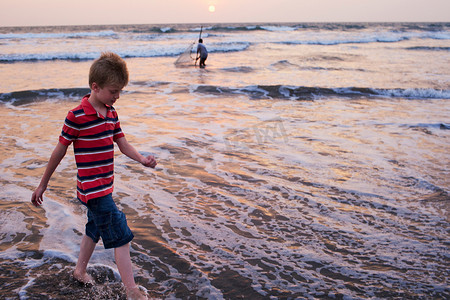 为爱而行摄影照片_男孩在沙滩上踏浪而行